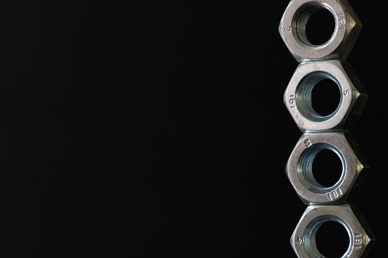 Detailed photo of four stacked hex nuts against a black background highlighting industrial design.