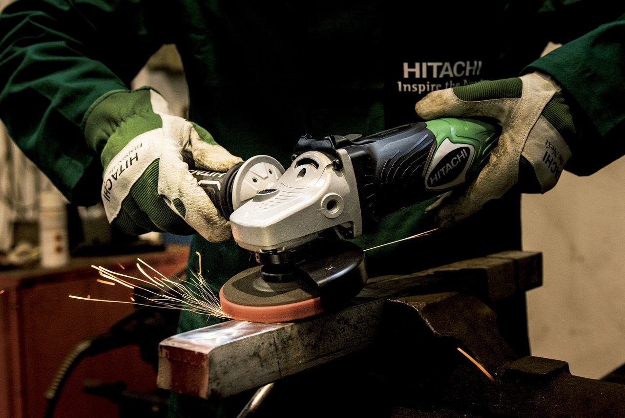 Worker using a grinder tool on metal, creating sparks. Safety gear and precision in industrial setting.