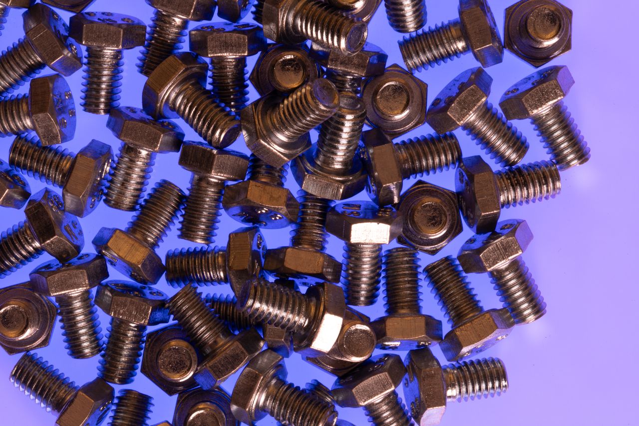 A scattered pile of shiny steel bolts on a vibrant purple surface, emphasizing industrial hardware.